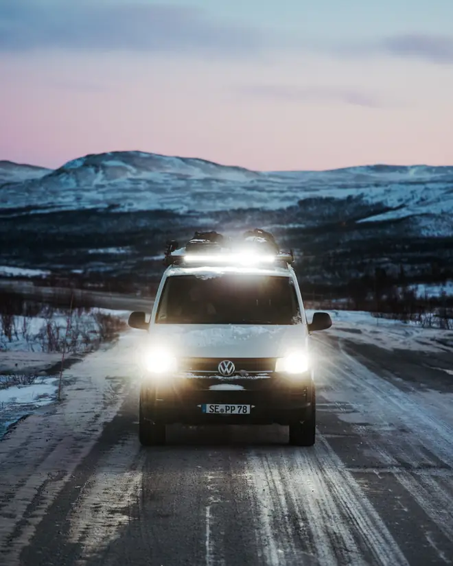 Der weiße VW T6 mit Dachscheinwerfern auf einer verschneiten Straße in der Dämmerung